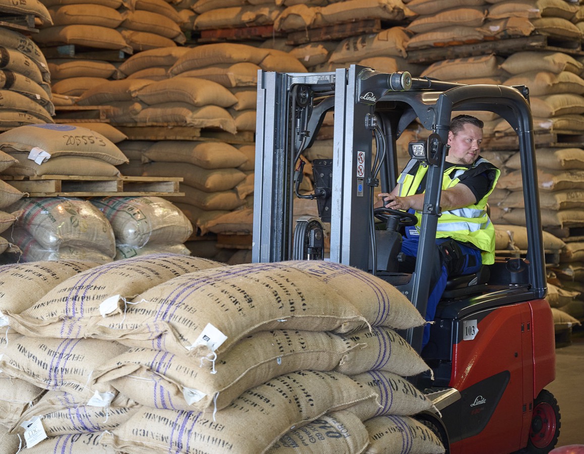 A forklift stacking jute sacks of green coffee in a warehouse.