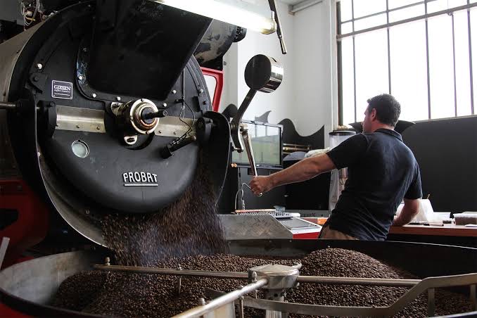 Roasted coffee dropping into the cooling tray beside the roaster's controls.