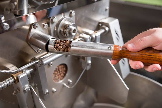 A roaster drawing a trier of beans from the drum of a shop roaster.