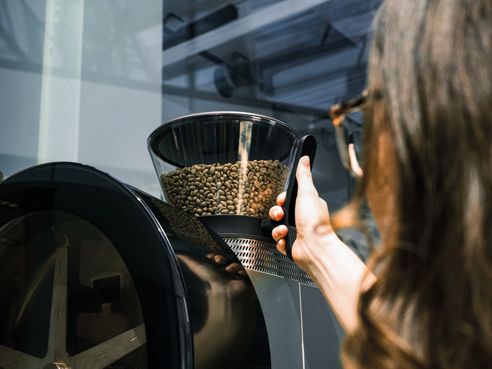 A roaster loading green coffee into the hopper of a drum roaster.